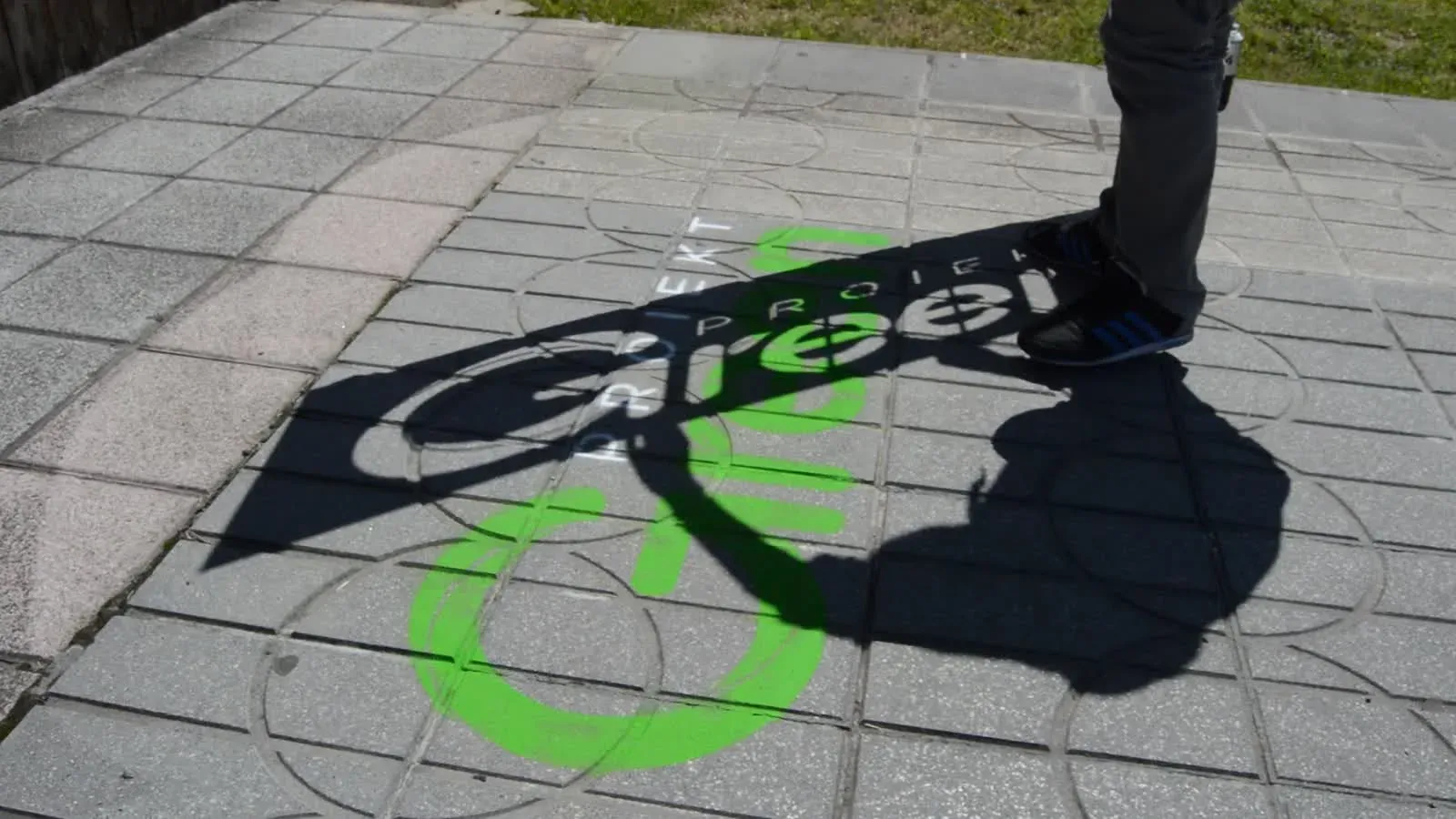 Plantilla retirada para revelar un Graffiti de Tiza verde sobre el pavimento.